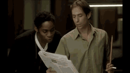 two men are standing next to each other in a pool room . one of the men is holding a pool cue .
