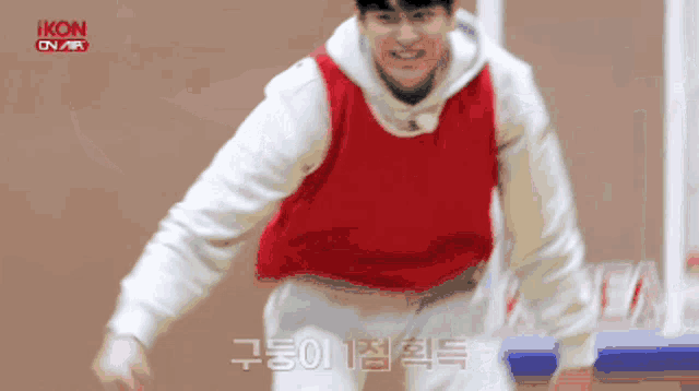 a man wearing a red vest and a white hoodie is standing in front of a basketball hoop .