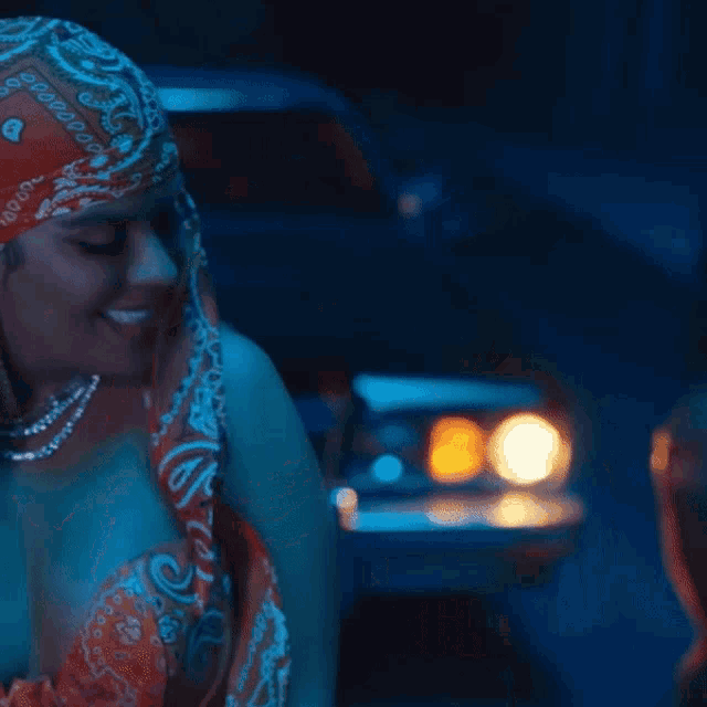 a woman wearing a bandana and a necklace is smiling in front of a car