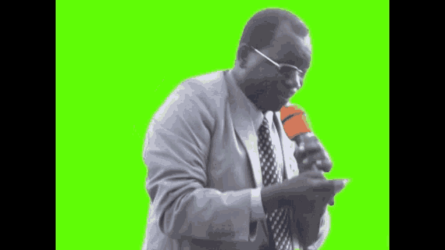 a man in a suit and tie is holding a microphone in front of a green screen