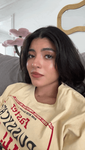 a woman sitting on a couch wearing a yellow t-shirt that says ' xyz261 ' on it