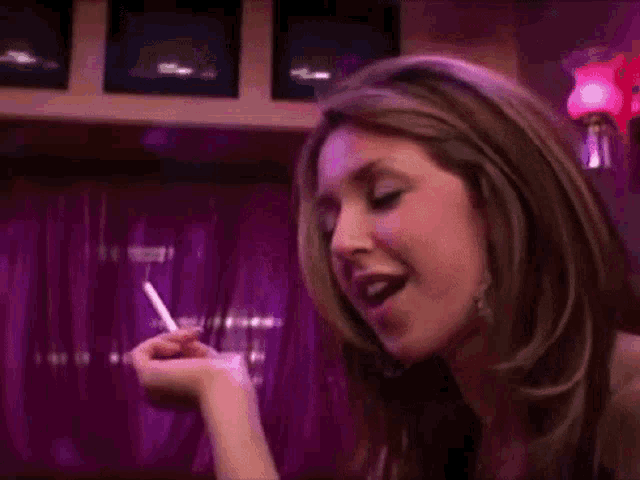 a woman is smoking a cigarette in a bar while talking on a cell phone .