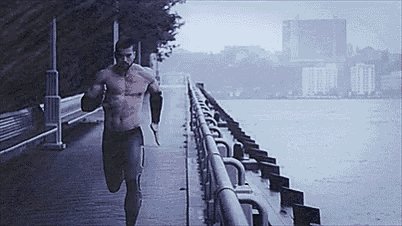 a shirtless man is running on a pier next to a body of water in the rain .