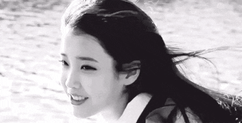a black and white photo of a woman with long hair standing on the beach .