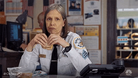 a police officer is sitting at a desk eating a hamburger .