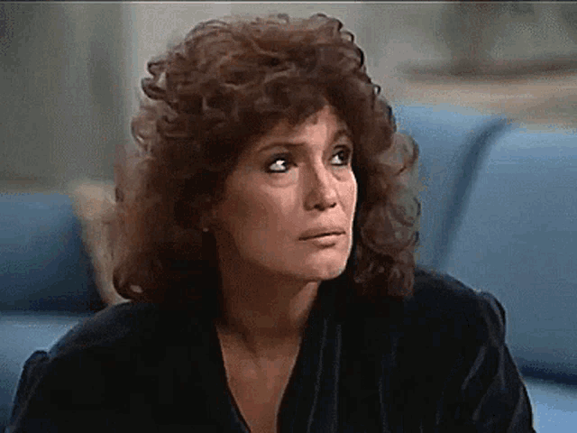 a woman with curly hair is sitting on a blue couch and looking at the camera