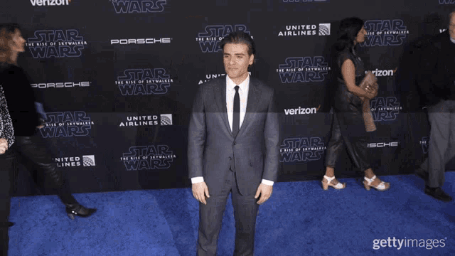 a man in a suit and tie stands on a blue carpet with star wars advertisements on it