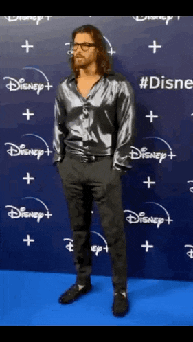 a man in a silver shirt and black pants is standing in front of a wall that says disney on it