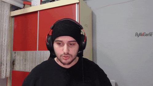 a man wearing headphones is standing in front of a wall that says bynogame