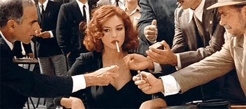 a woman is smoking a cigarette while surrounded by men in suits .