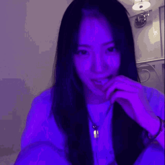 a woman with long black hair is wearing a white shirt and a purple light is shining on her face .
