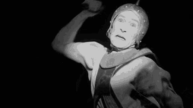 a black and white photo of a man in a costume holding a sword in his hand .