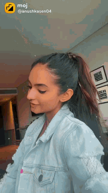 a woman wearing a denim jacket and a ponytail has a moji icon on her face