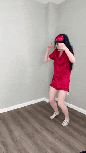 a woman in a red pajamas and sleep mask is dancing in a room .