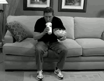 a man is sitting on a couch eating chips and drinking a cup