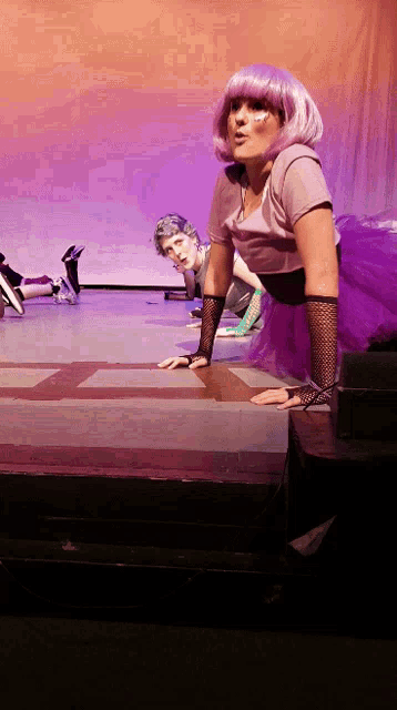 a woman in a purple wig crawls on the floor