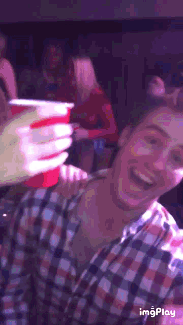 a man in a plaid shirt holds up a red cup
