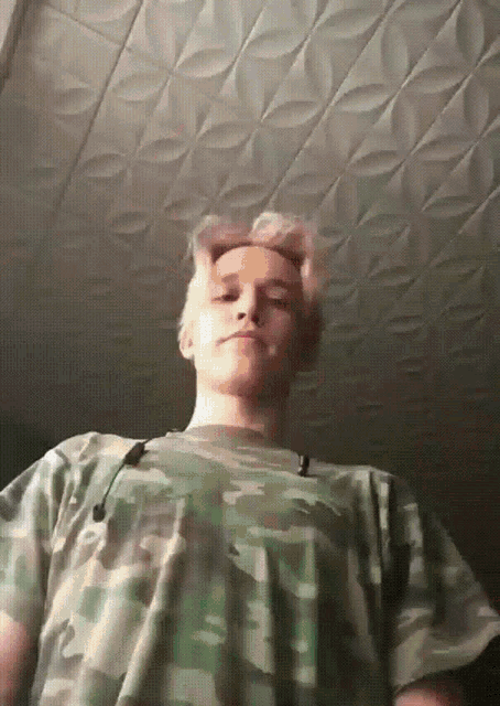 a man wearing a camouflage shirt is looking down at the camera