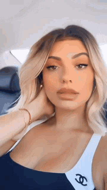 a woman in a black and white tank top with a chanel logo on it is taking a selfie in a car .