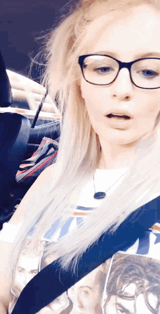 a woman wearing glasses and a shirt with a picture of a man on it is sitting in a car