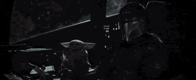 a baby yoda is sitting on a person 's lap in a dark room .