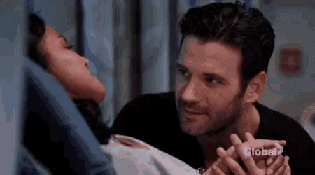 a man and a woman are holding hands in a hospital room while the woman is laying in bed .