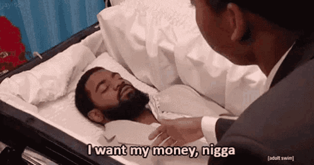 a man in a suit is laying in a coffin with the words `` i want my money , nigga '' .