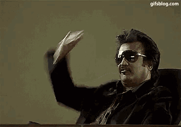 a man wearing sunglasses is sitting at a desk with the word adhu written on the bottom