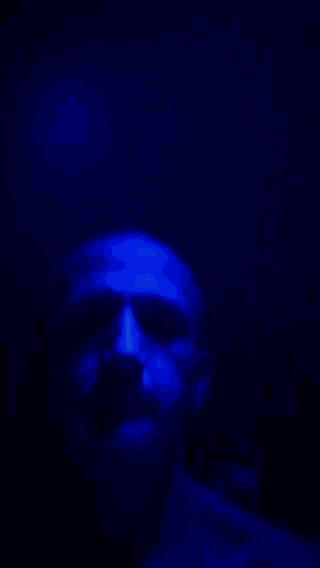 a close up of a man 's face in a dark room with blue lights behind him .