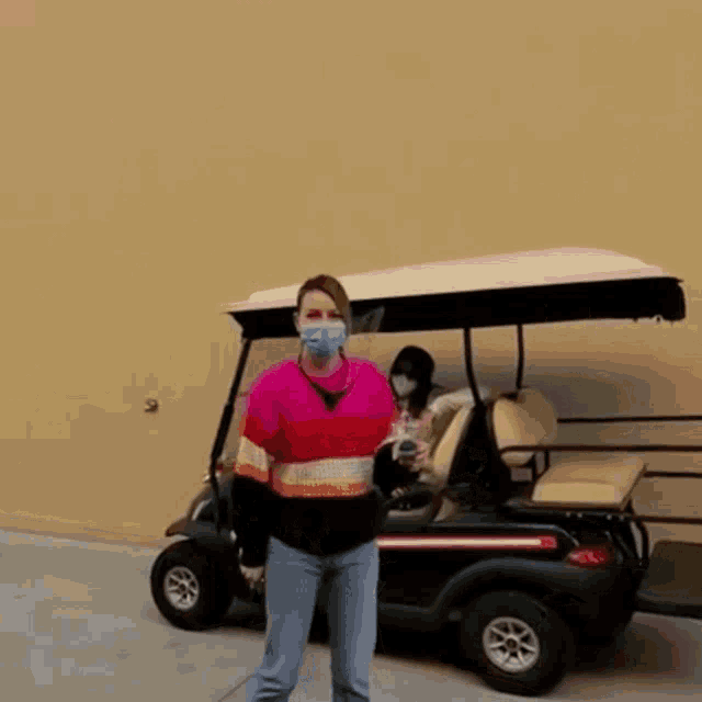 a woman wearing a face mask is standing in front of a golf cart