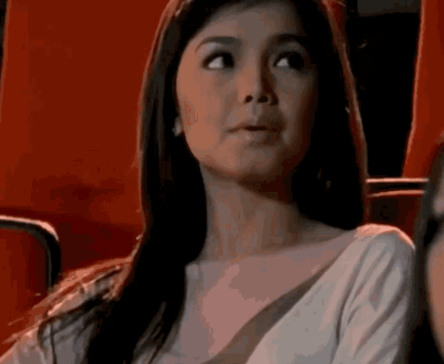 a woman in a white shirt is sitting in a red chair with her mouth open