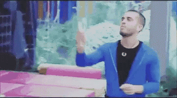a man in a blue jacket and black shirt is standing in front of a pink couch .