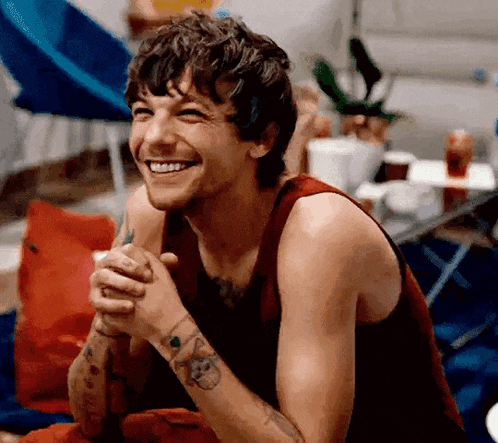 a man in a red tank top is smiling with his hands folded in prayer .