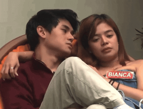 a man and a woman are sitting next to each other and the woman is wearing a bianca tag