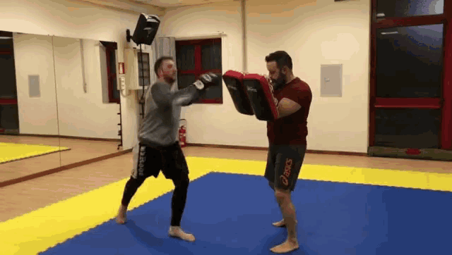 a man wearing a pair of asics shorts is boxing with another man