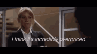 a woman in a suit says i think it 's incredibly overpriced in front of a man