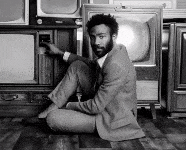 a man in a suit is sitting in front of a stack of old televisions including one that says u.s. army