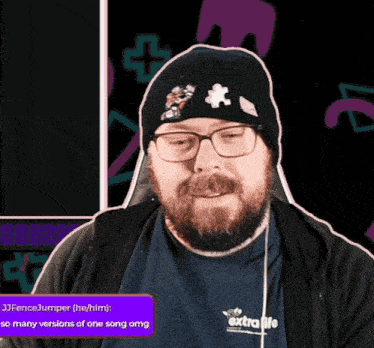 a man with a beard and glasses is wearing a black beanie and a blue shirt that says extra life