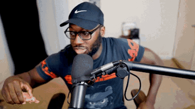 a man wearing a nike hat and glasses is eating a piece of pizza in front of a microphone