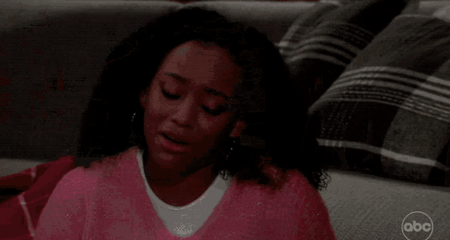 a woman in a pink sweater is laying on a couch with abc written on the corner