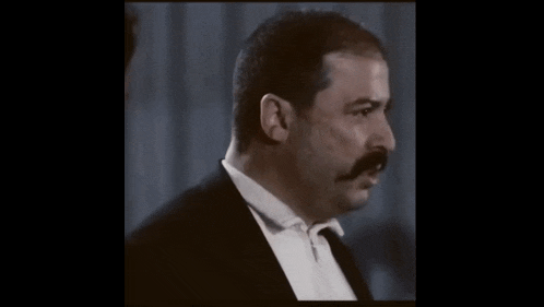 a man with a mustache is talking to another man in a tuxedo .