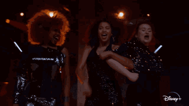 three women are dancing in a dark room with a disney logo in the corner