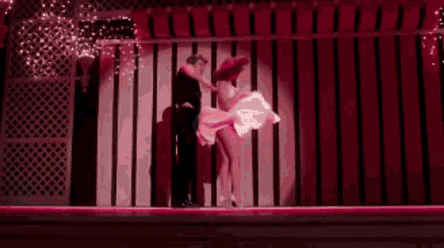 a man and a woman are dancing in a dark room with pink lights .