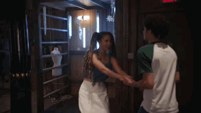 a man and a woman are dancing in a dark room with a red exit sign in the background