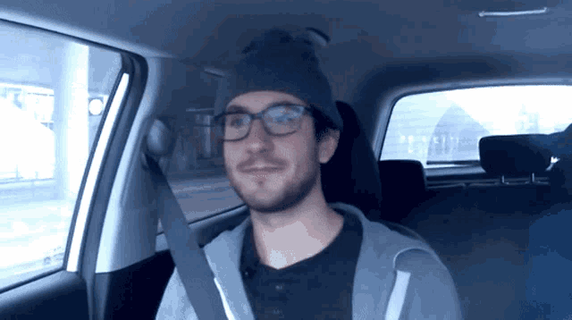a man in a car wearing glasses and a beanie