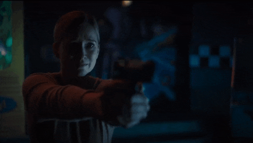 a woman is pointing a gun at the camera in a dark room