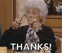an elderly woman is sitting at a table holding a pair of glasses and saying `` thanks ! ''