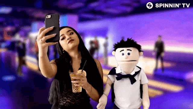 a woman taking a selfie next to a puppet with spinnin ' tv in the background