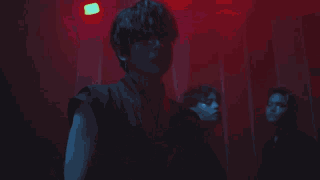 a man with glasses holds his hand to his head in a dark room with red lights