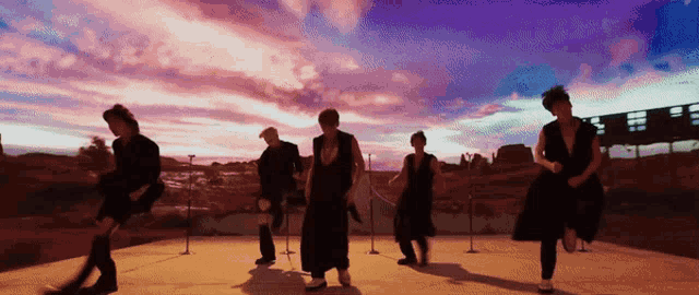 a group of people dancing in front of a sunset